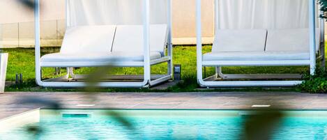 Two white lounge chairs with metal frames, positioned on a tiled patio next to a swimming pool.