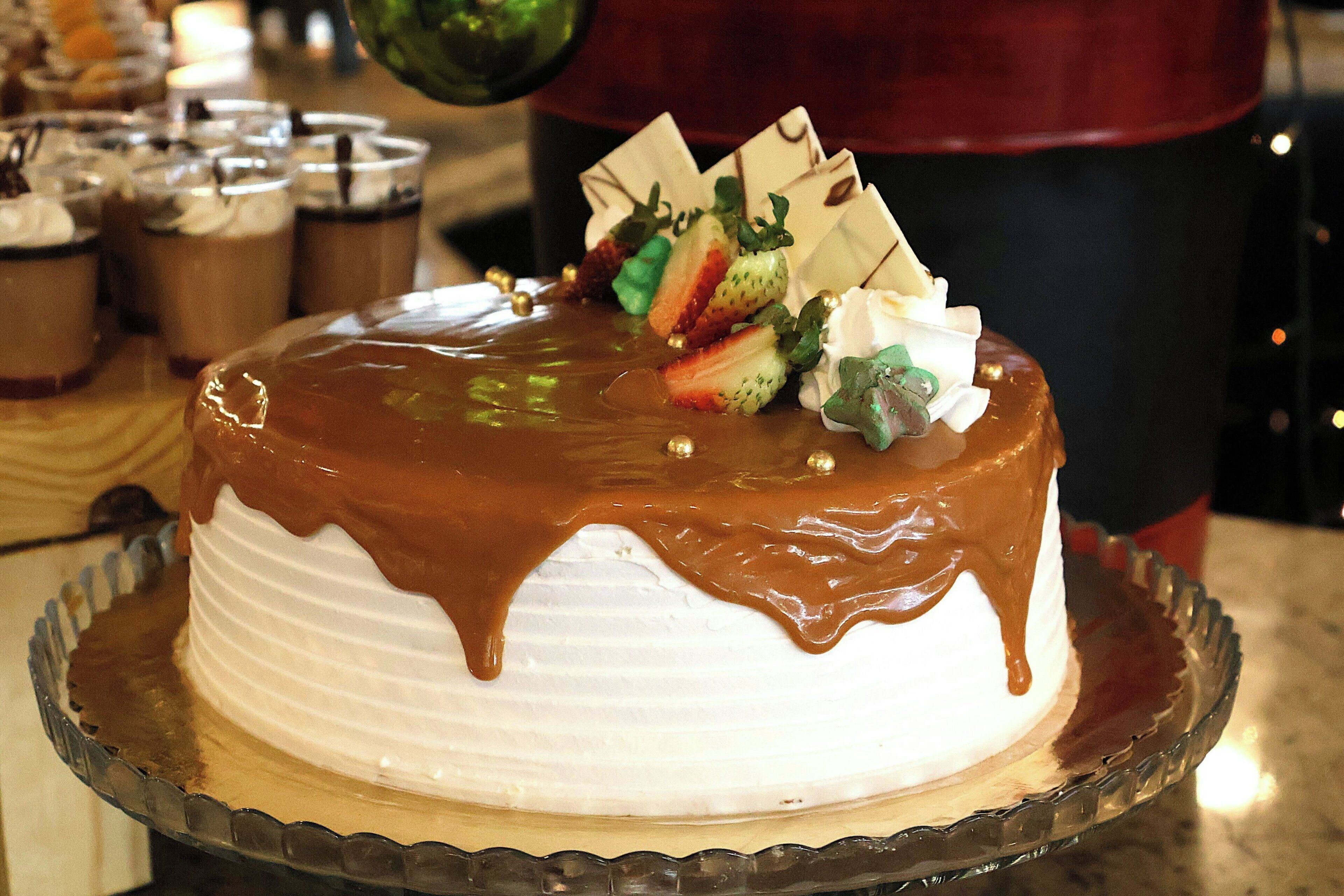 A cake with white frosting and chocolate drizzle on a glass plate.