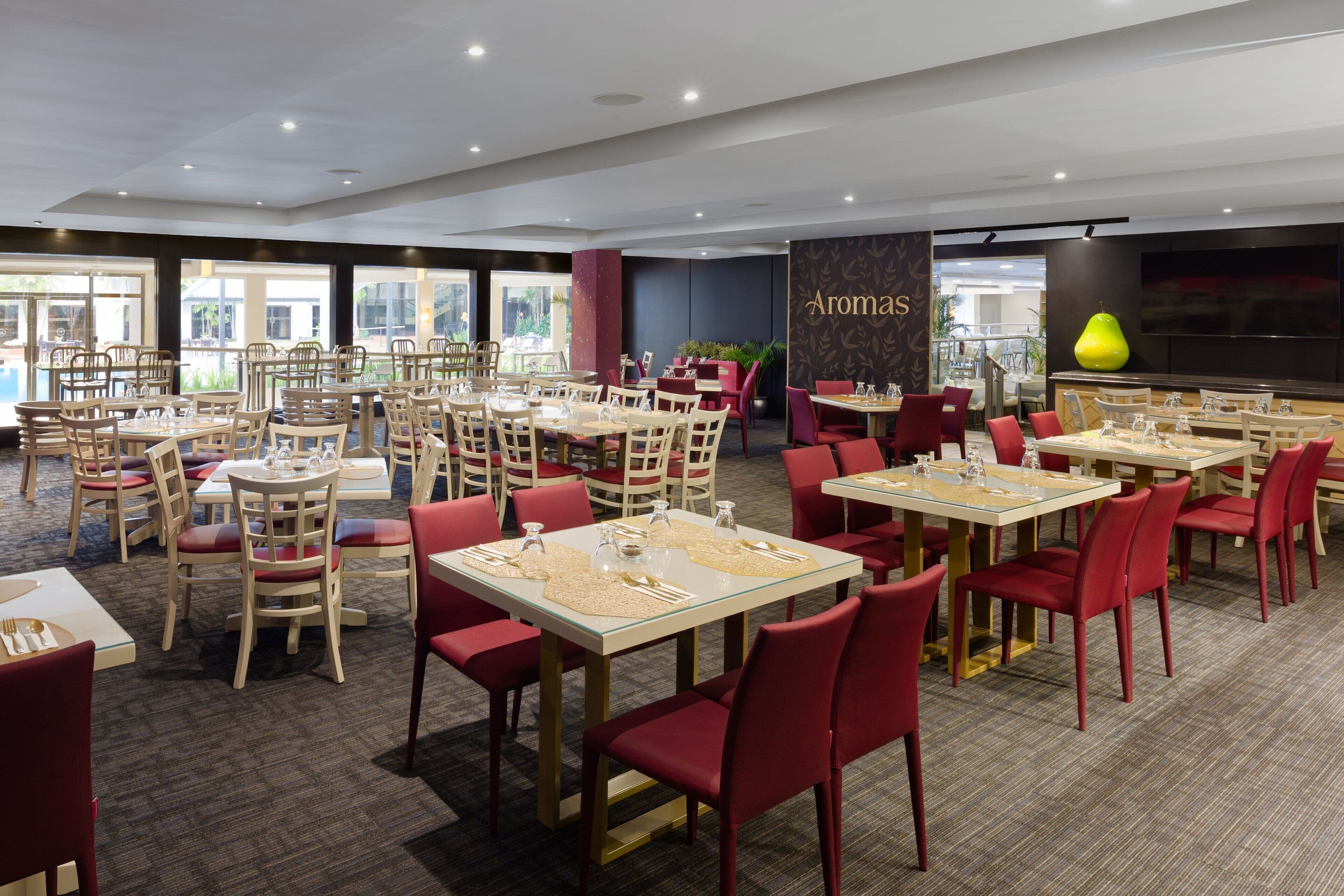 A spacious dining area with multiple tables and chairs, large windows, and a wall with the word "Aromas".
