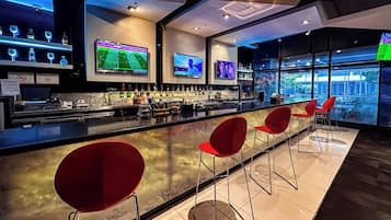 Et moderne barområde med flere fjernsyn, der viser sportsbegivenheder, en velassorteret bar og røde barstole.