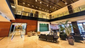 A spacious lobby with a high ceiling, a glass railing on the upper level, and a seating area with modern furniture.