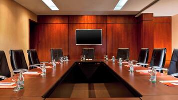 Un salón de conferencias con una larga mesa, sillas de cuero negro, un televisor de pantalla plana y botellas de agua sobre la mesa.