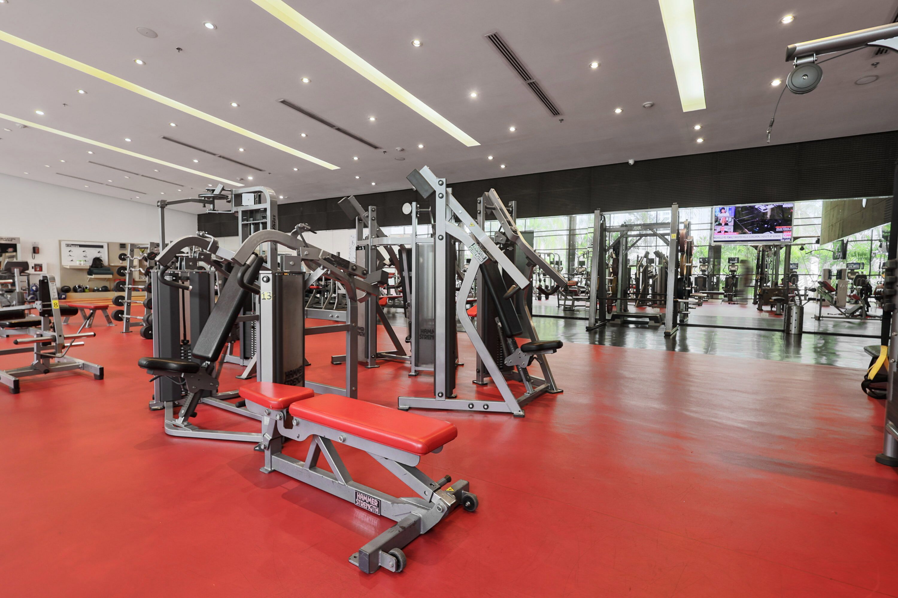 Een sportschool met diverse fitnessapparaten, een rode vloer en een grote spiegel die de apparatuur weerspiegelt.