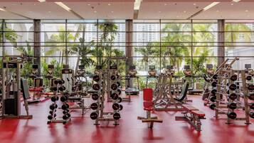 A gym with various exercise equipment, large windows, and a red floor.