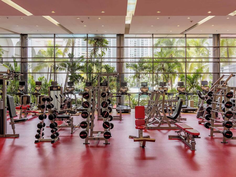 A gym with various exercise equipment, large windows, and a red floor.