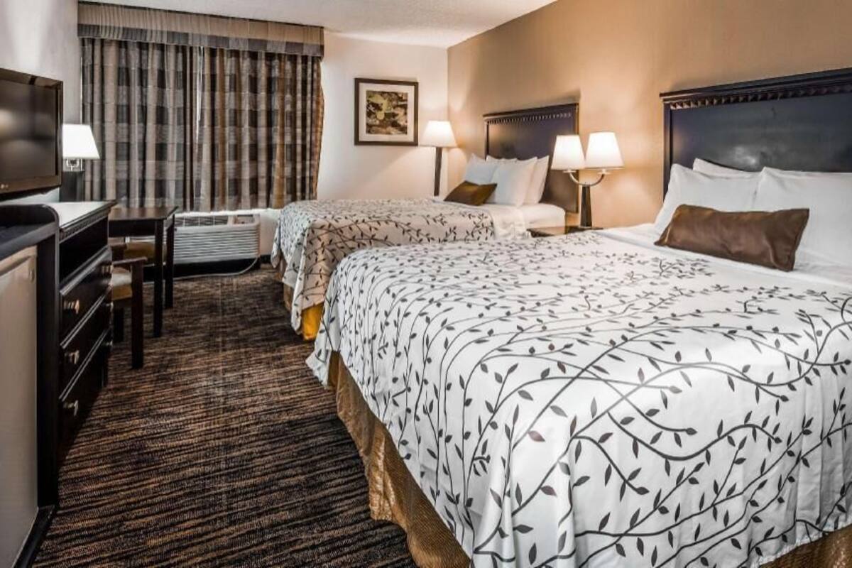 A hotel room with two beds, a TV, a desk, and a large window with curtains.
