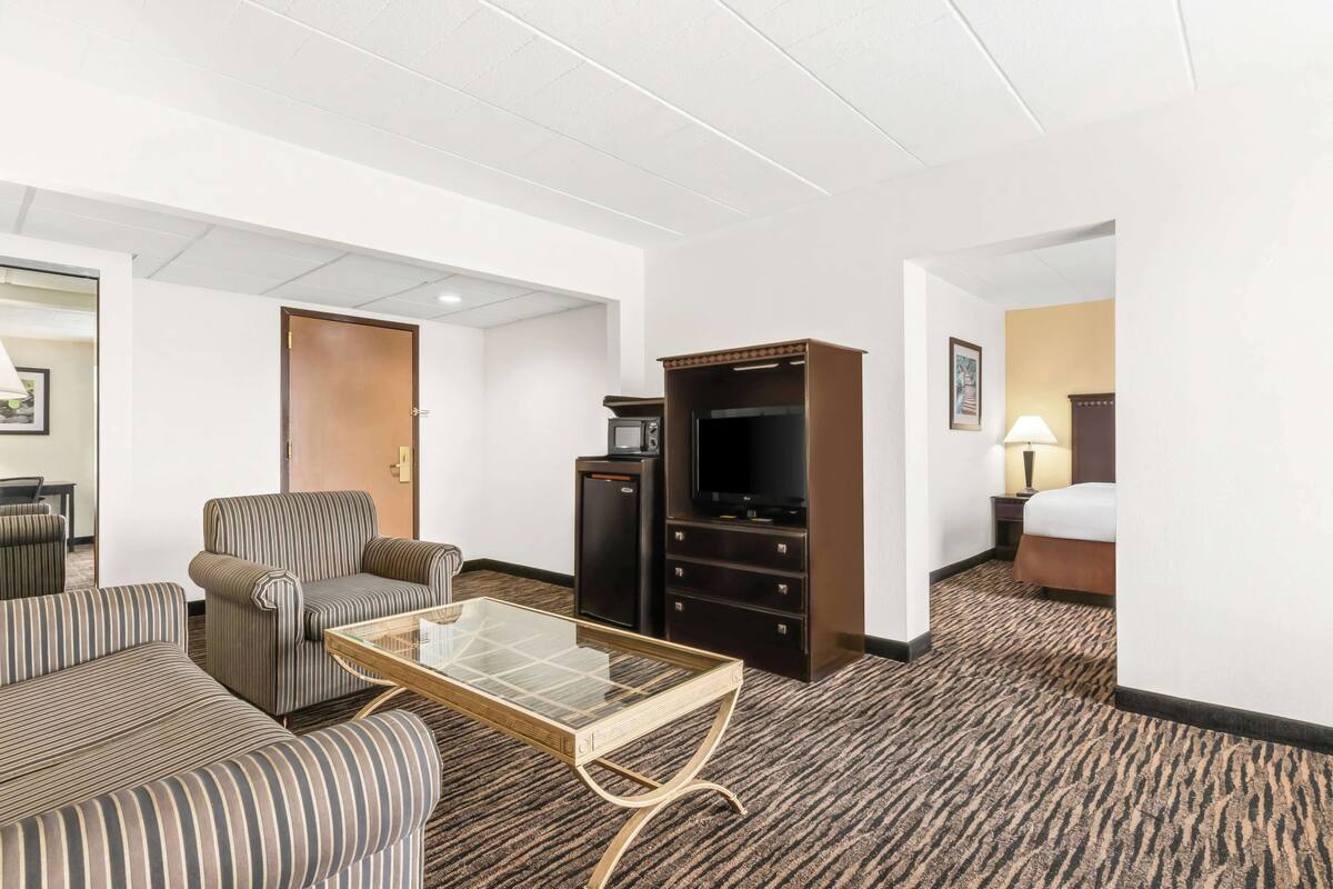A hotel room with a striped sofa, a glass-top coffee table, a television, a minibar, and a bed.