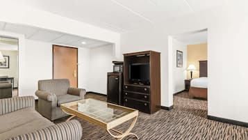 A hotel room with a striped sofa, a glass-top coffee table, a television, a minibar, and a bed.