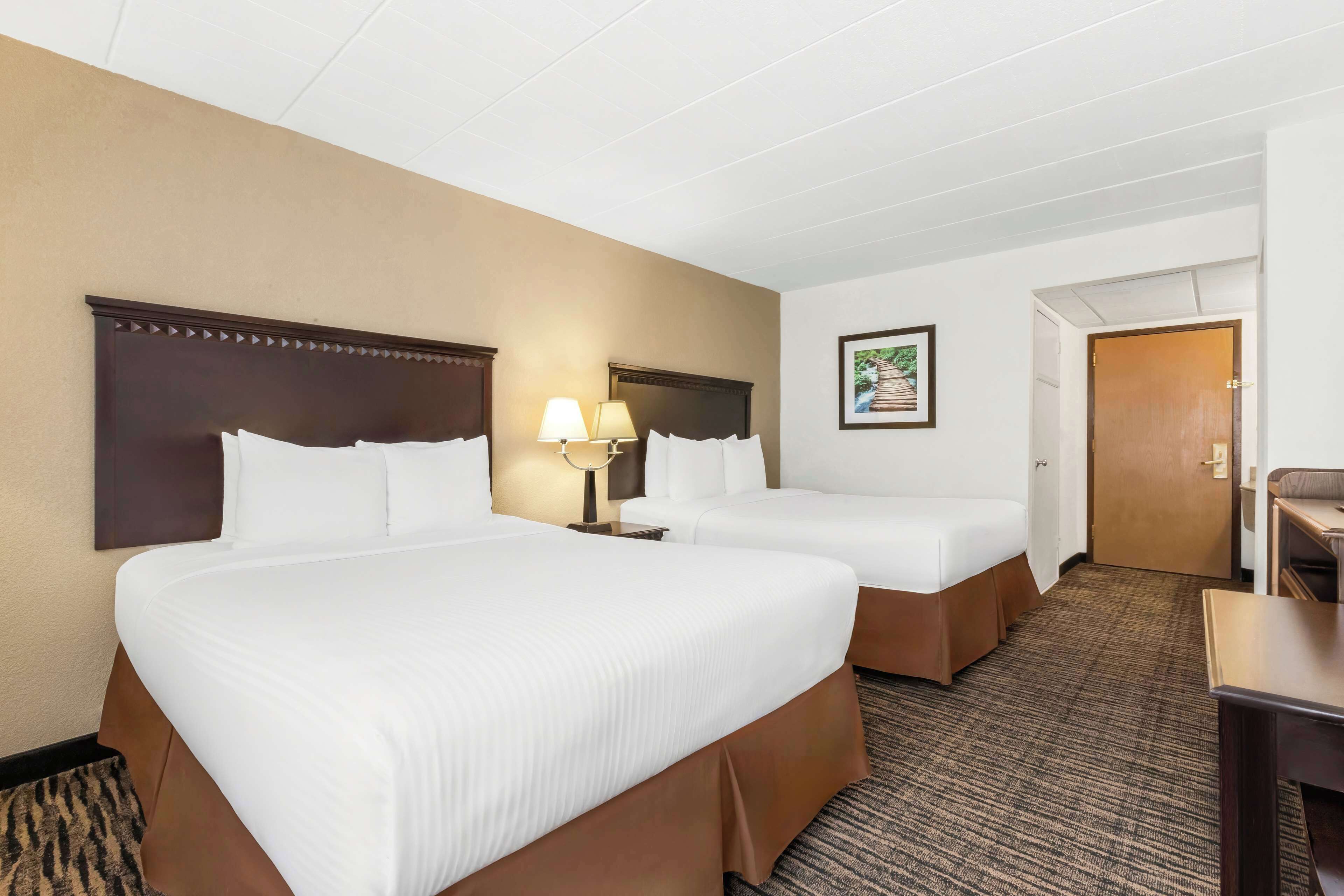 A hotel room with two beds, a desk, and a door.