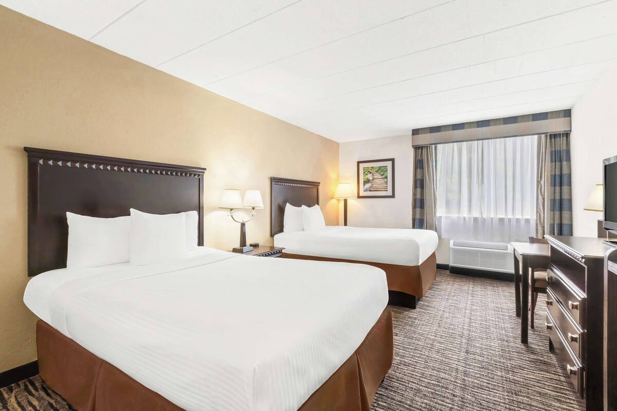 A hotel room with two beds, a desk, a chair, a television, and a window with curtains.