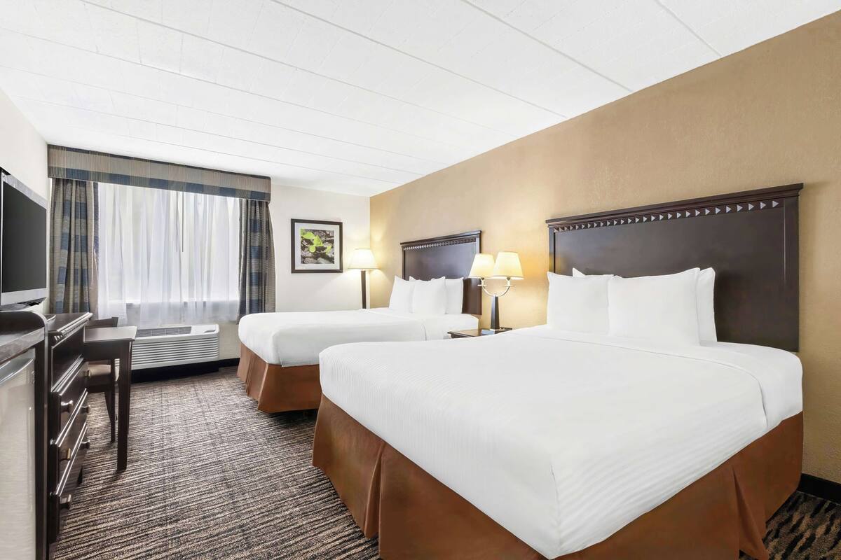 A hotel room with two beds, a desk, a TV, and a window with curtains.