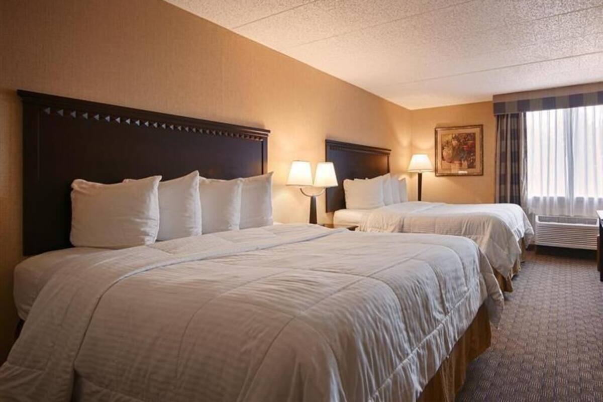 A hotel room with two beds, a headboard, bedside lamps, a painting, and a window with curtains.