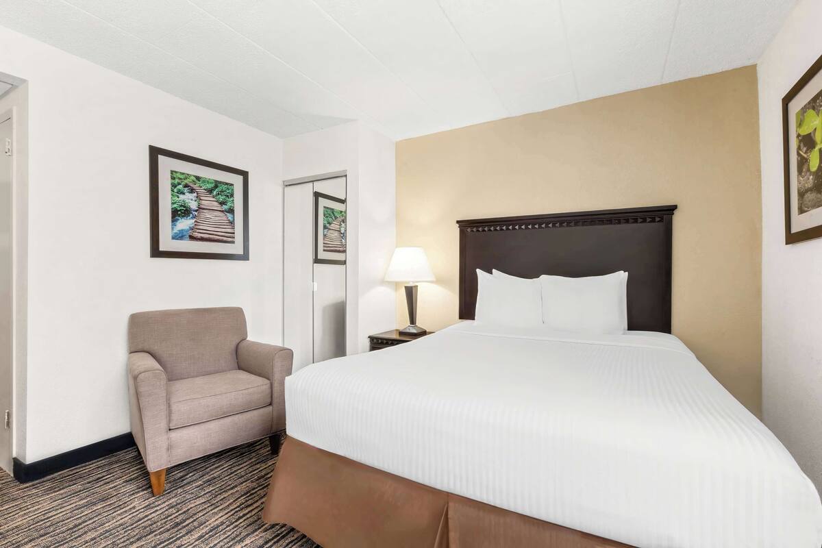 A hotel room with a large bed, a chair, a nightstand with a lamp, and framed pictures on the walls.