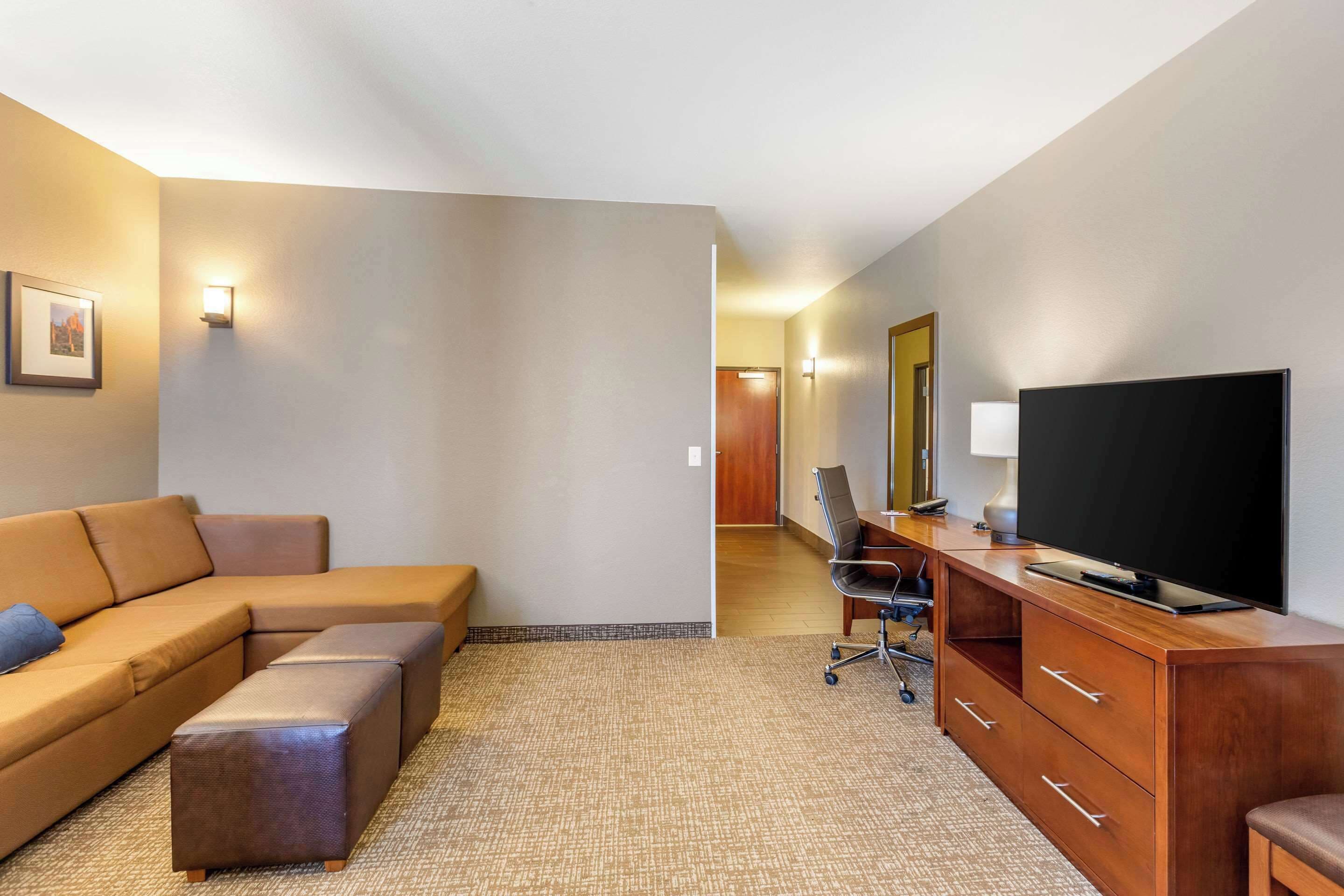Habitación de hotel con sofá modular, televisor de pantalla plana, escritorio con silla y un espejo grande.