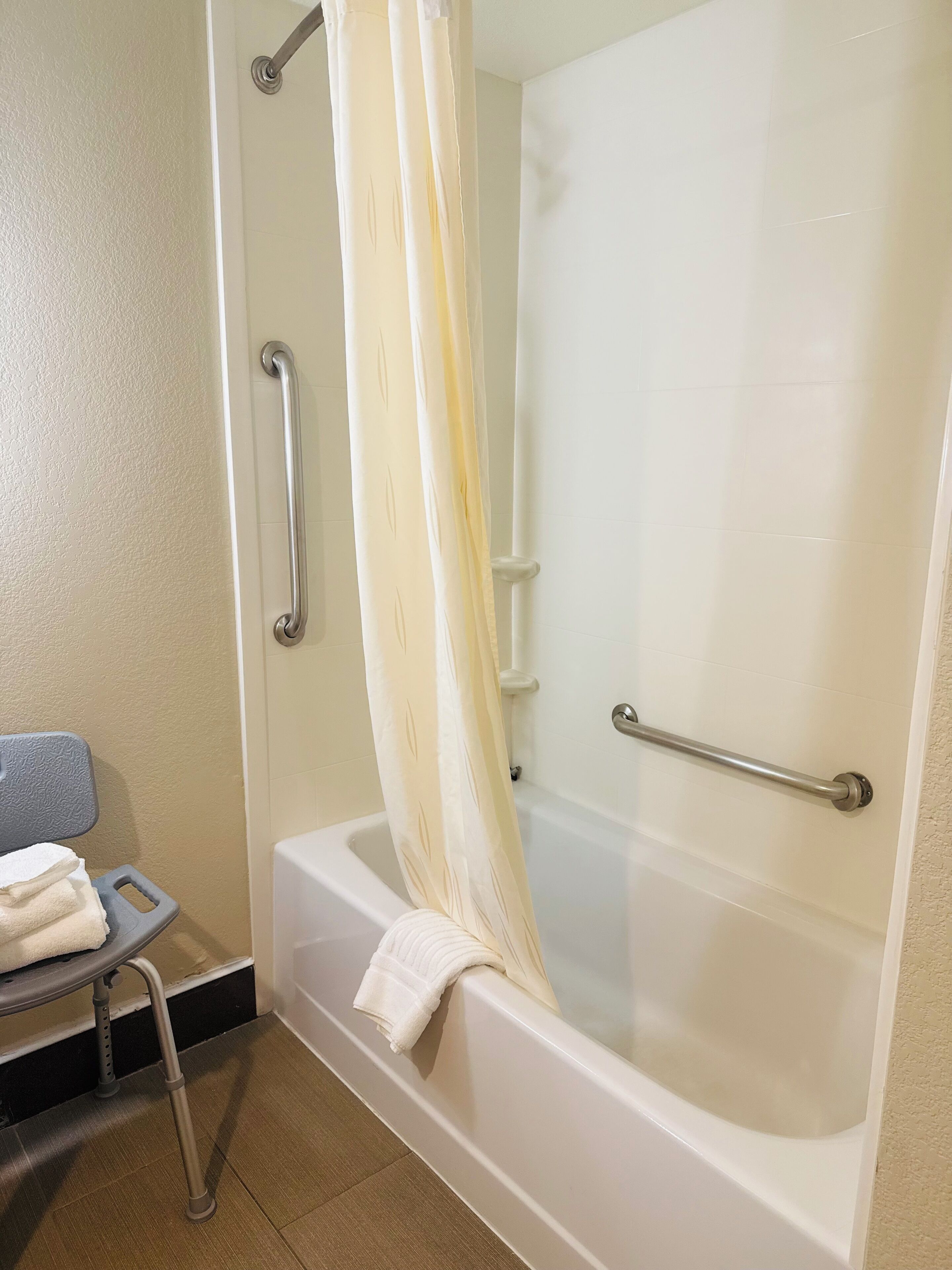 A bathroom with a bathtub, grab bars, a shower curtain, and a towel rack.