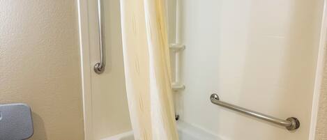 A bathroom with a bathtub, grab bars, a shower curtain, and a towel rack.