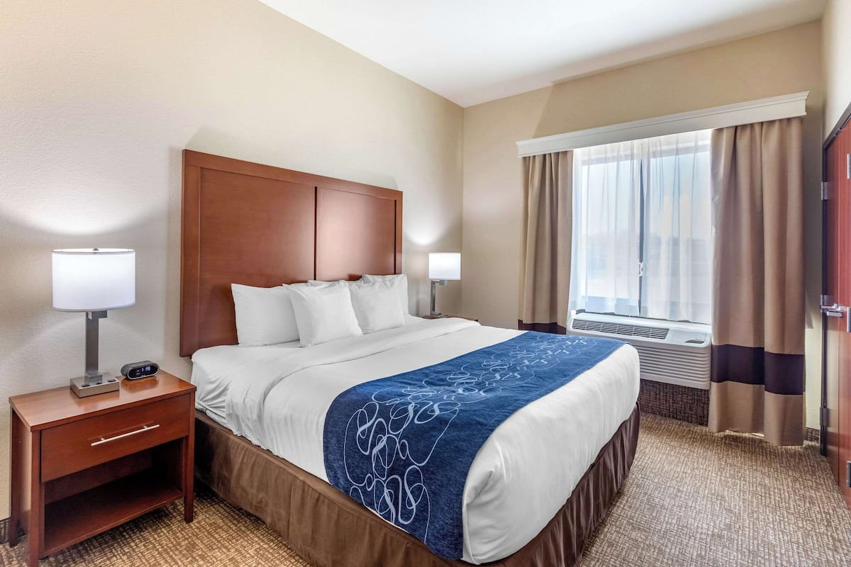 A hotel room with a large bed, two bedside tables, a nightstand, a window with curtains, and a door.