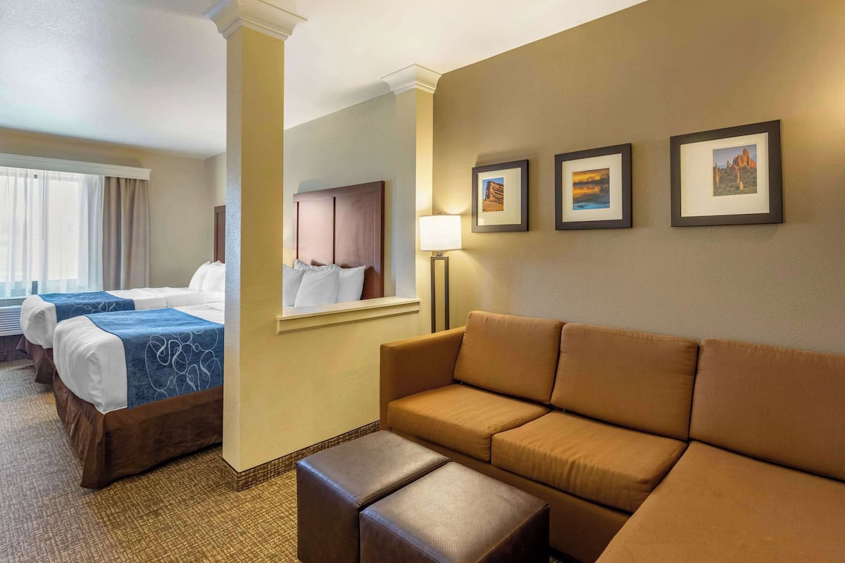 A hotel room with a sofa, two beds, a lamp, and three framed pictures on the wall.