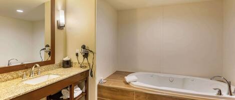 A modern bathroom with a granite countertop sink, a large mirror, a wooden vanity, and a freestanding bathtub.