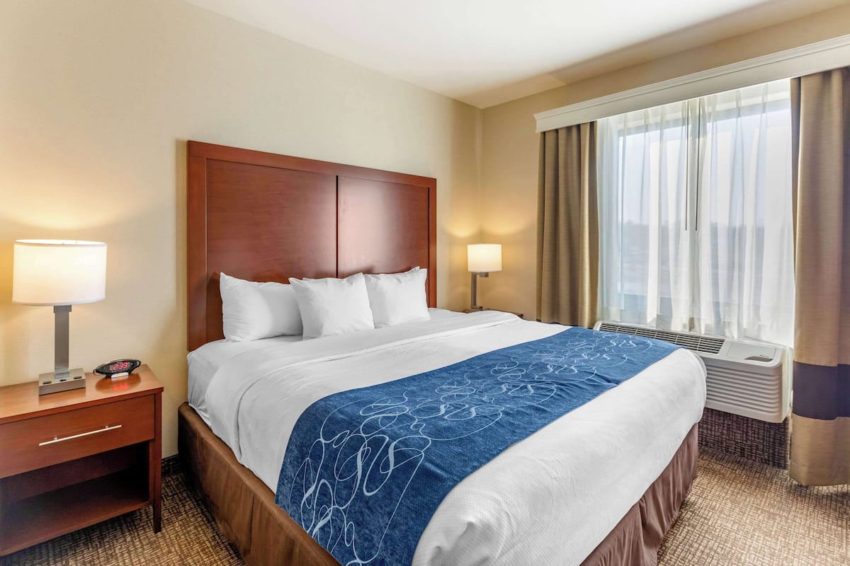 A hotel room with a large bed, two bedside lamps, a nightstand, and a window with curtains.