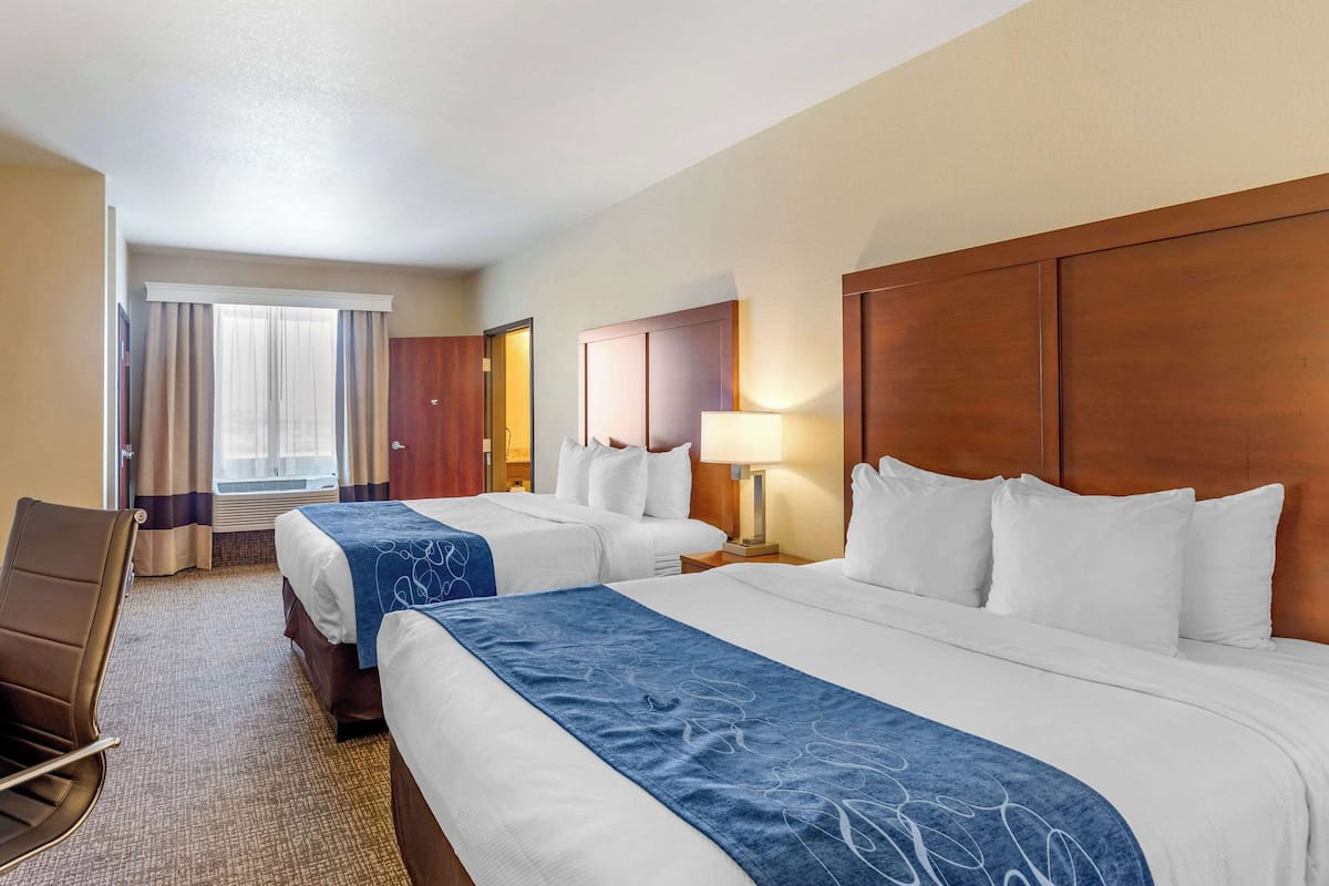 A hotel room with two beds, a desk, and a chair.