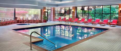 Una piscina interior con sillas reclinables rojas y una pared de ladrillo.