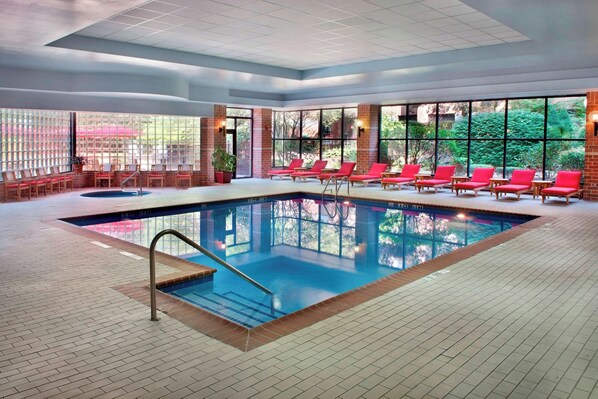 An indoor swimming pool with red lounge chairs and a brick wall.