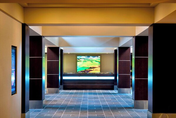 A modern hotel lobby with a large digital screen displaying a scenic view, a tiled floor, and dark-toned walls. - Trumbull Marriott Shelton (Trumbull)