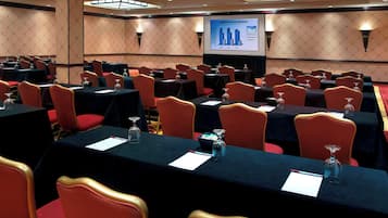 A conference room with multiple tables, red chairs, and a presentation screen displaying a financial summary.