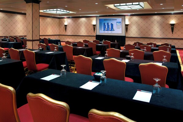 Un salón de conferencias con varias mesas, sillas rojas y una pantalla mostrando un resumen financiero.