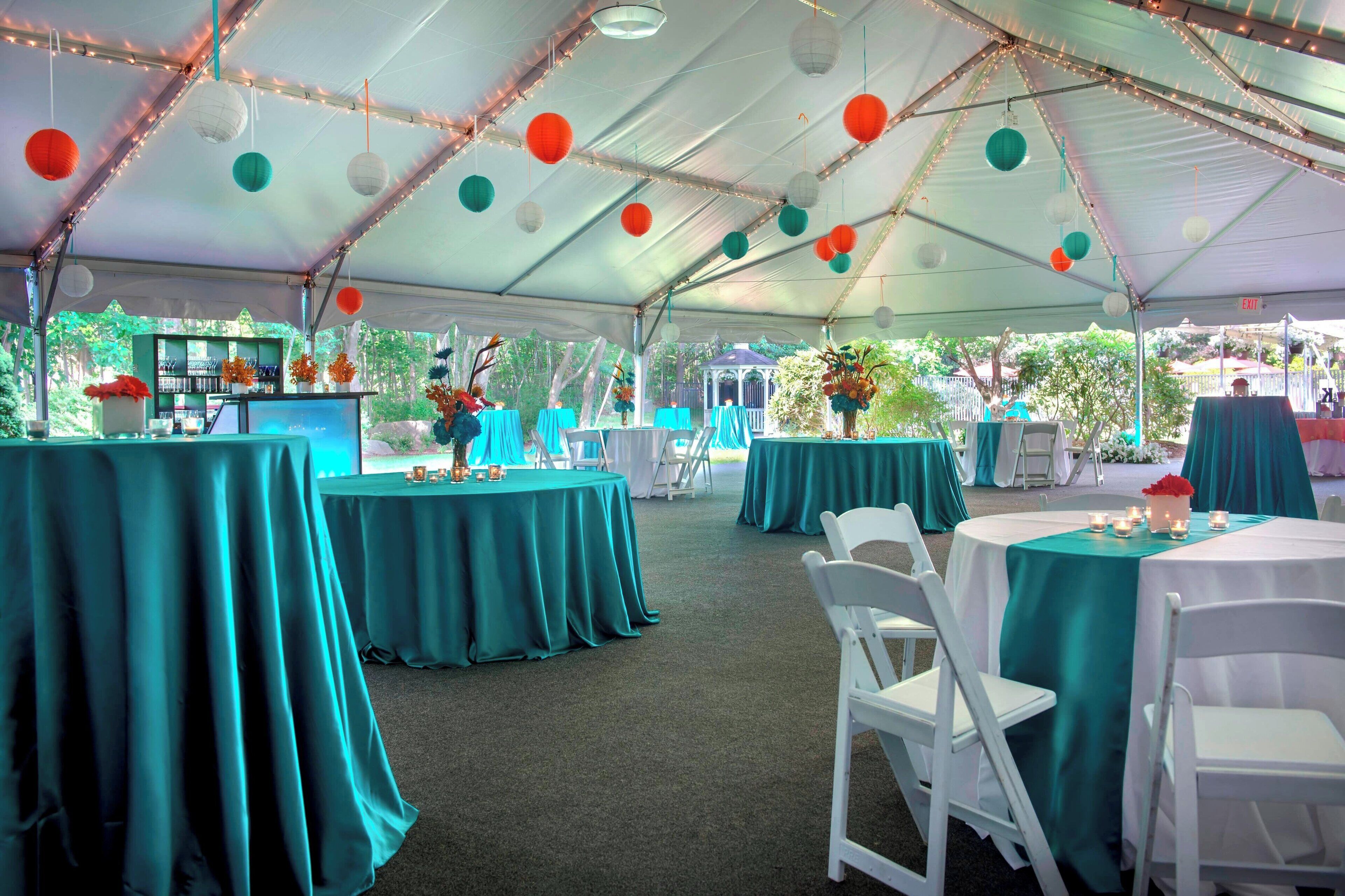 A tented event space with tables covered in teal tablecloths, white chairs, and string lights.