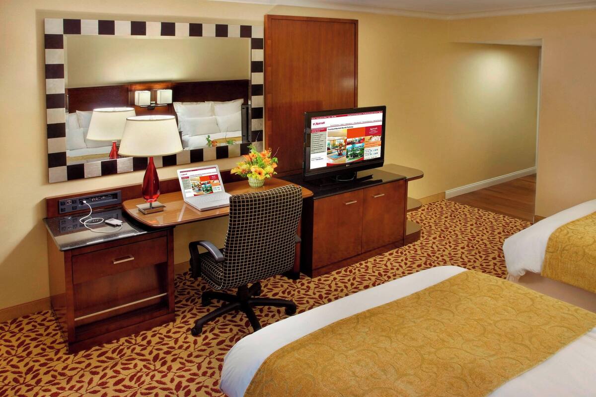 A hotel room with a bed, a desk with a computer, a chair, a TV, and a mirror.