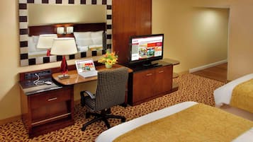Quarto de hotel com uma cama, uma mesa com computador, uma cadeira, uma TV e um espelho.