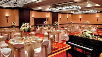 A banquet hall with round tables set for a formal event, featuring white tablecloths, floral centerpieces, and a grand piano.