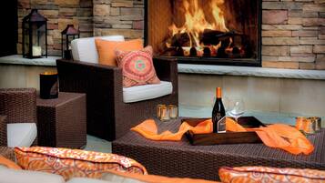 A cozy outdoor seating area with wicker furniture, a fireplace, and a bottle of champagne.
