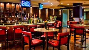 Una zona de bar con sillas rojas, un televisor montado en la pared y estanterías con botellas.