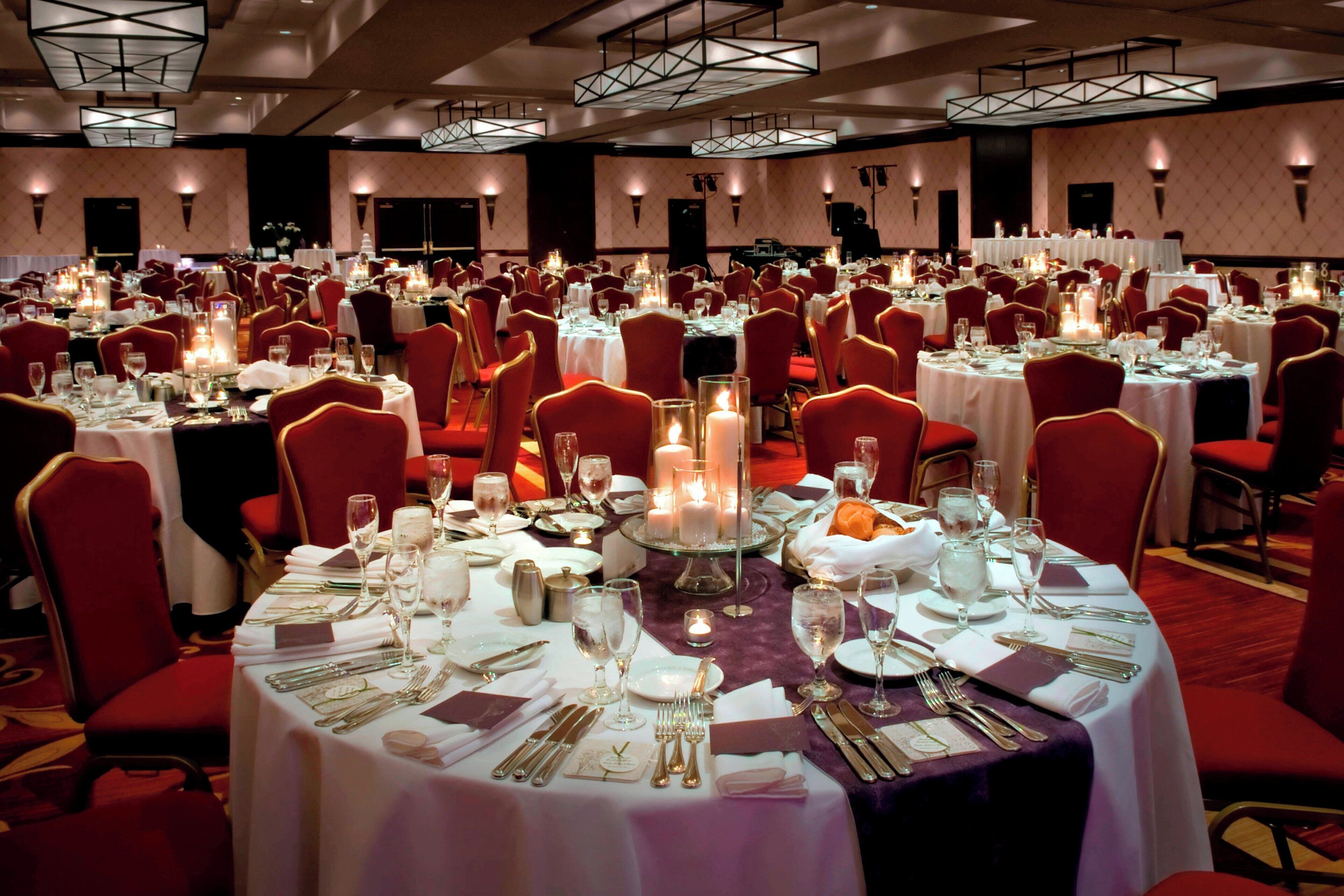 A banquet hall with round tables set for dining, red upholstered chairs, and candlelit centerpieces.