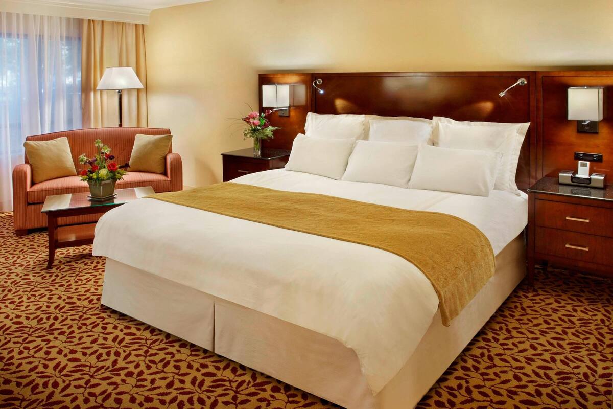 A hotel room with a large bed, a sofa, a nightstand, and a lamp.