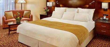 Quarto de hotel com uma cama grande, um sofá, uma mesa de cabeceira e uma luminária.