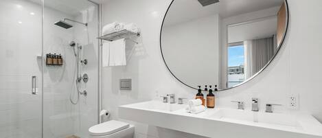 A modern bathroom with a glass shower enclosure, a white sink with a large mirror, and toiletries on the counter.