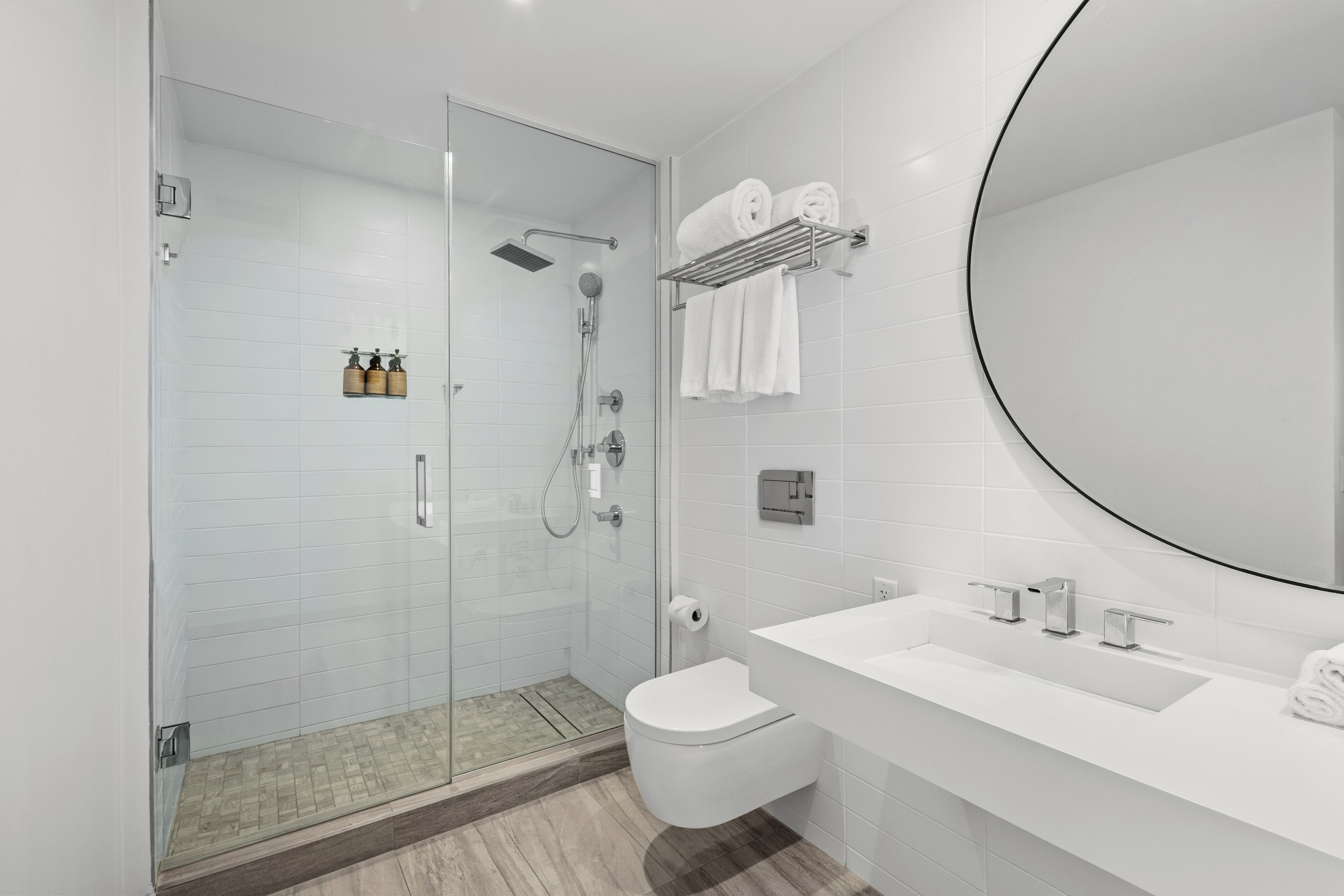 Een moderne badkamer met een douchecabine van glas, een wit wastafelmeubel met een grote spiegel, en netjes opgevouwen handdoeken op een plank.