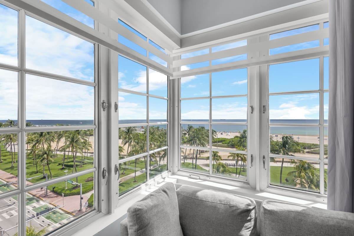 Ein Zimmer mit großen Fenstern und Blick auf Strand und Palmen.