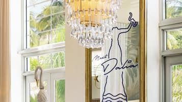 Una habitación con ventanas amplias, una escultura decorativa de un pájaro, un candelabro y un espejo con la inscripción 'Meet Paula'.