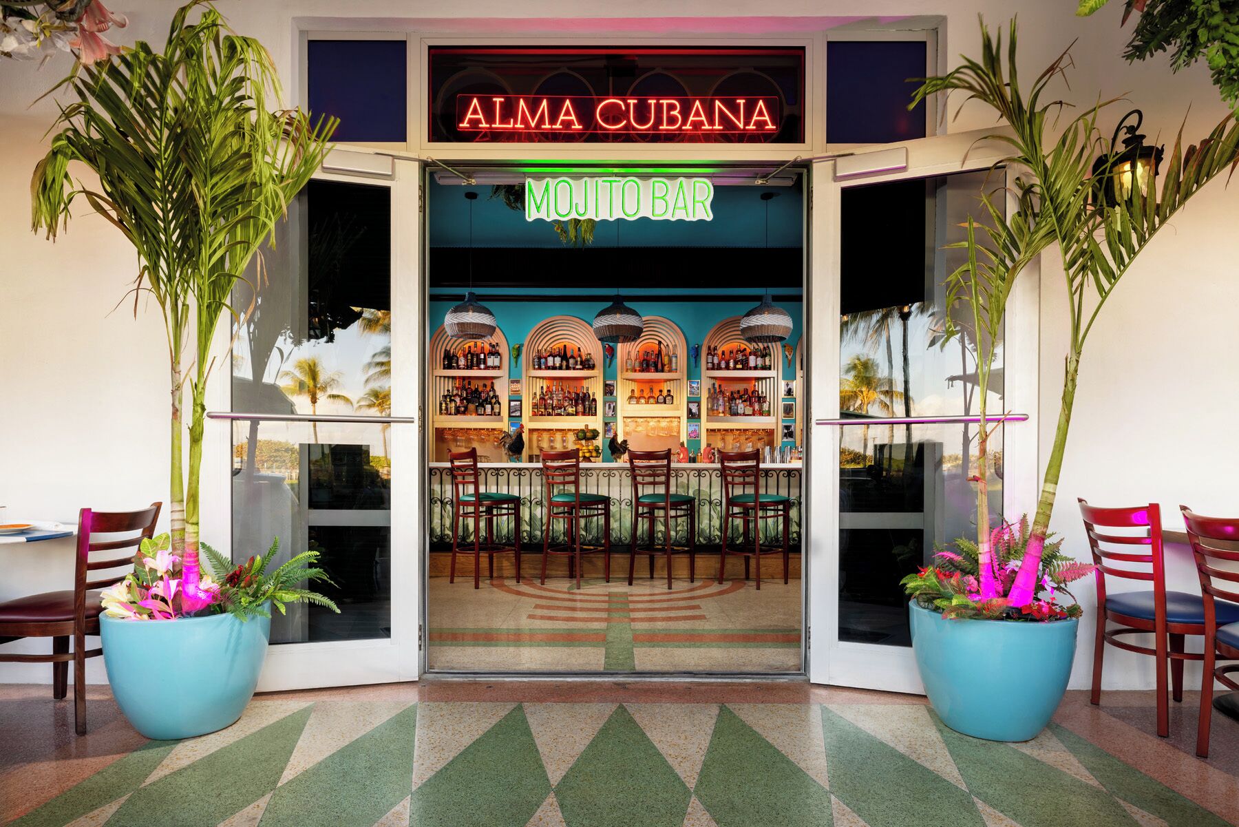 The entrance of Alma Cubana, featuring a mojito bar with a tropical decor and large potted plants.