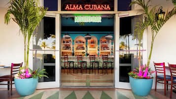 The entrance of Alma Cubana, featuring a mojito bar with a tropical decor and large potted plants.
