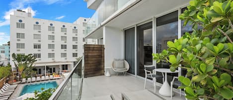 A modern balcony with a pool, lounge chairs, and a dining area.