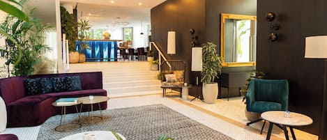 A spacious living area with a sofa, coffee table, and chairs, a staircase leading to a dining area, and a large mirror on the wall.