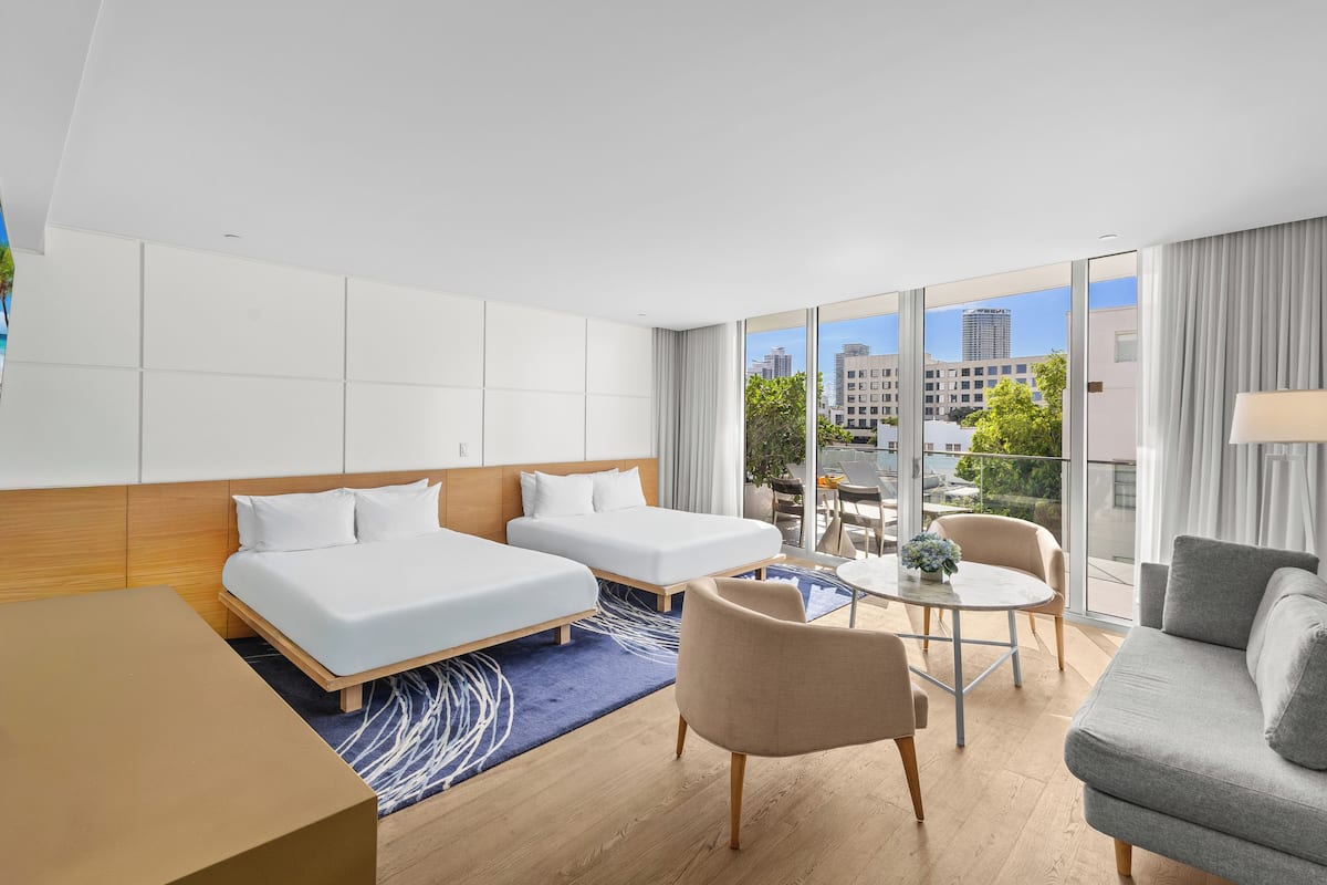 Ein modernes Hotelzimmer mit zwei Betten, einem Sofa, einem kleinen Tisch und Blick auf die Stadt.