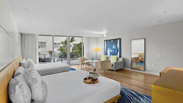 Une chambre d’hôtel avec deux lits, un bureau, une chaise, une lampe et une grande fenêtre donnant sur l’extérieur.