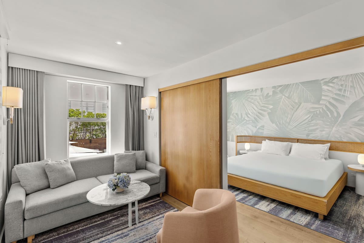 Ein modernes Hotelzimmer mit einem großen Bett, einer Couch, einem kleinen Tisch und Blick auf Grünflächen.